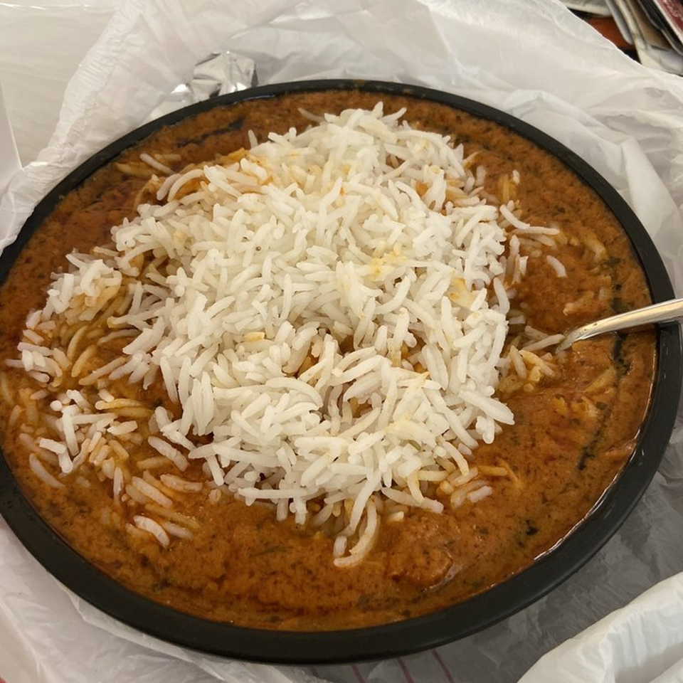 Tandoori House's Indian curry dish with white rice, served in a black bowl with a spoon.