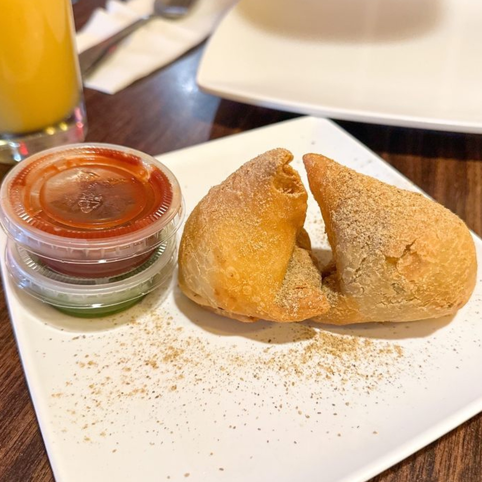 Two golden-brown samosas dusted with spices, served with dipping sauces on a white plate at Tandoori House.