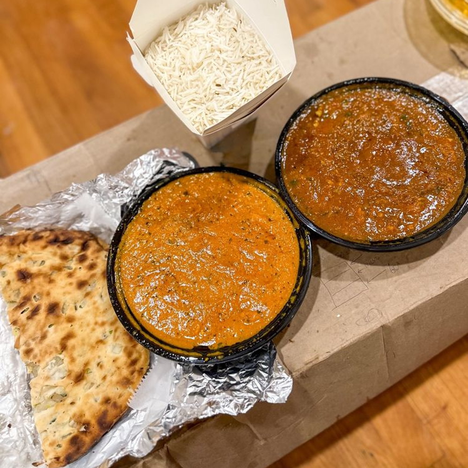 Tandoori House Indian takeout with two curries, basmati rice, and naan bread on a cardboard box.