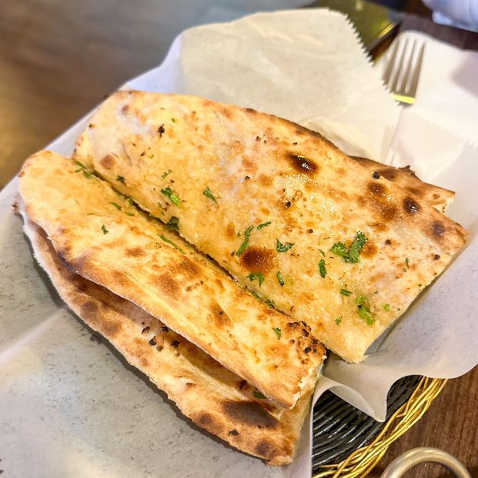 Golden brown garlic naan bread, garnished with green herbs, served in a basket at Tandoori House.