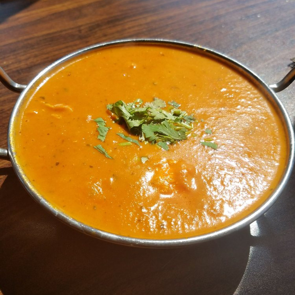 A metal bowl of orange Indian curry, garnished with fresh green cilantro, on a wooden table.