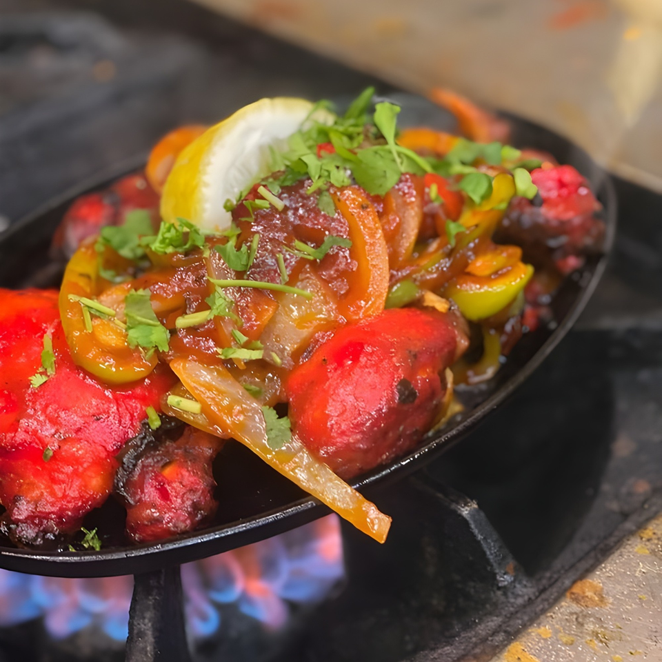 Sizzling Tandoori chicken with onions, peppers, and cilantro, garnished with a lemon wedge.