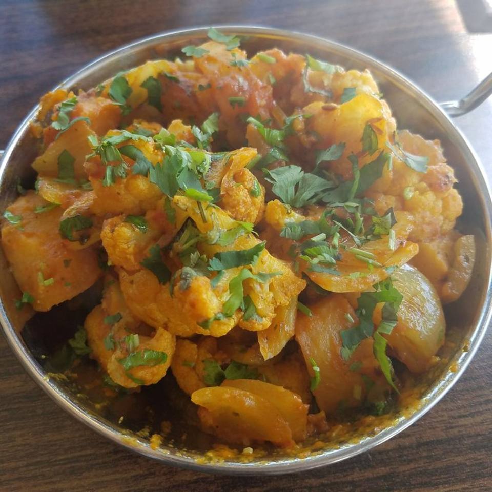 A close-up of Aloo Gobi, an Indian dish with potatoes and cauliflower, garnished with fresh cilantro.