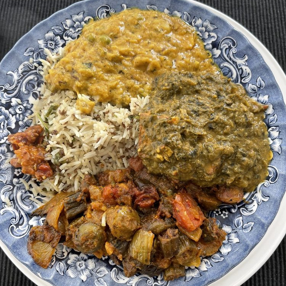 A blue and white plate filled with Tandoori House's Indian rice, dal, saag, and mixed vegetables.
